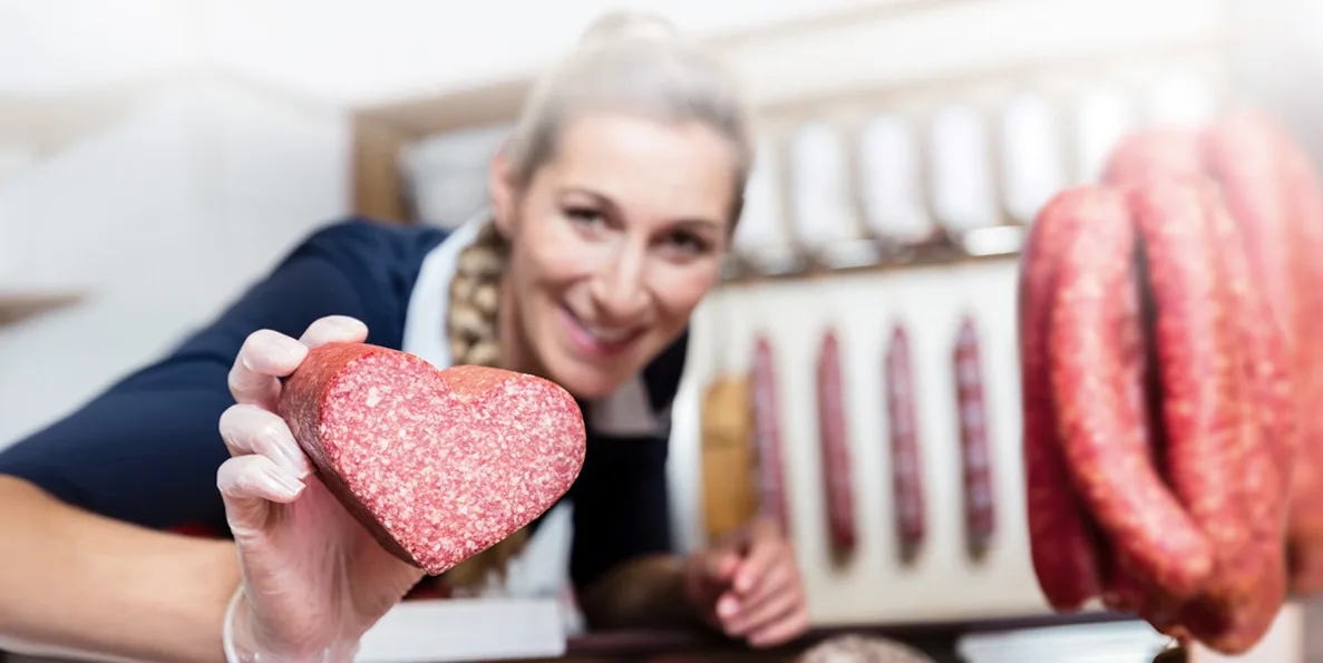 Verkäuferin präsentiert herzförmige Salami und Würste an der Theke